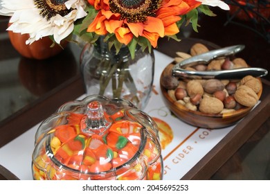 The Top Down, Close Up Image Of A Fall Themed Table Setting. A Bouquet Of Orange Sunflowers, A Bowl Filled With Mixed Nuts In The Shell, And A Glass Cookie Jar Filled With Candy Corn Sit In A Tray.