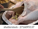 The top down, close up image of a man stuffing a turkey with a wooden spatula.
