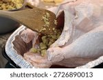 The top down, close up image of a man stuffing a turkey with a wooden spatula.