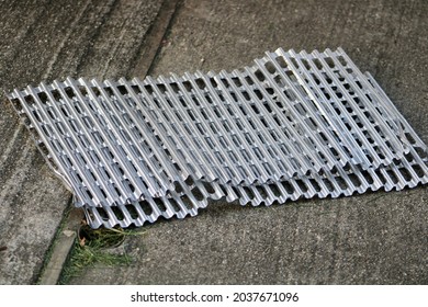 The Top Down, Close Up View Of Aluminum Grate Covers Laying On A Cement Patio In A Suburban Backyard. They're Used As A Sanitary Cover For The Grill On A Barbecue.