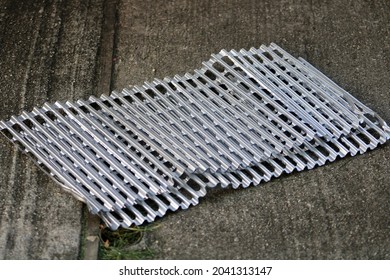 The Top Down, Close Up View Of Aluminum Grate Covers Laying On A Cement Patio In A Suburban Backyard. They're Used As A Sanitary Cover For The Grill On A Barbecue.