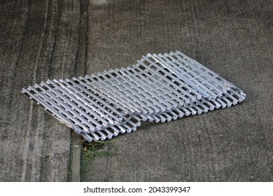 The Top Down, Close Up View Of Aluminum Grate Covers Laying On A Cement Patio In A Suburban Backyard. They're Used As A Sanitary Cover For The Grill On A Barbecue.