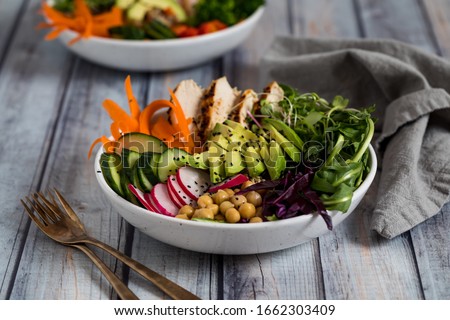 A top down close up view of a buddha bowl filled with various vegetables and grilled chicken. Healthy eating concept.