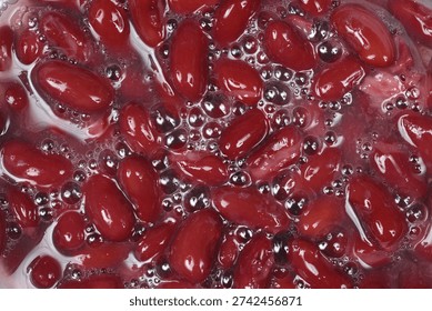 A top down close up view of dark red kidney beans soaking in water with small bubbles on the surface