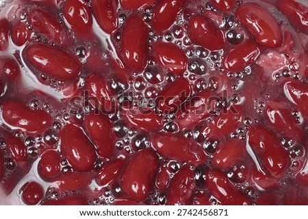 A top down close up view of dark red kidney beans soaking in water with small bubbles on the surface