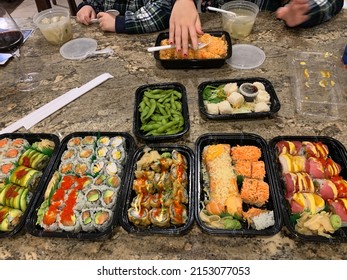 The Top Down, Close Up View Of A Family Eating A Sushi Dinner. There Are Different Types Of Rolls, Dumplings, Rice, Soups, And Edamames.