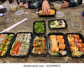 The Top Down, Close Up View Of A Family Eating A Sushi Dinner. There Are Different Types Of Rolls, Dumplings, Rice, Soups, And Edamames.