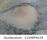 The top down, close up view of a giant pot hole that is filled with water from the melting snow bank in front of it.