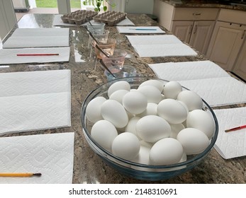 The Top Down, Close Up View Of A Kitchen Counter Set Up For Kids To Paint Easter Eggs. There Are Paper Towels, Paint Brushes, Empty Egg Cartons, Hard Boiled Eggs, And Dying Stations.