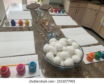 The Top Down, Close Up View Of A Kitchen Counter Set Up For Kids To Paint Easter Eggs. There Are Paper Towels, Paint Brushes, Paint Tubes, Empty Egg Cartons, Hard Boiled Eggs, And Dying Stations.