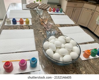 The Top Down, Close Up View Of A Kitchen Counter Set Up For Kids To Paint Easter Eggs. There Are Paper Towels, Paint Brushes, Paint Tubes, Empty Egg Cartons, Hard Boiled Eggs, And Dying Stations.