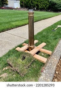 The top down, close up view of a mail box post being installed. The copper toned post is traditionally detailed. The grass is cut, a hole is dug, and anchors are being installed.