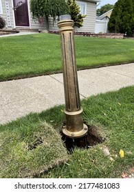 The top down, close up view of a mailbox post being installed. The copper toned post is traditionally detailed. The grass is cut, a hole is dug, and anchors are being installed.