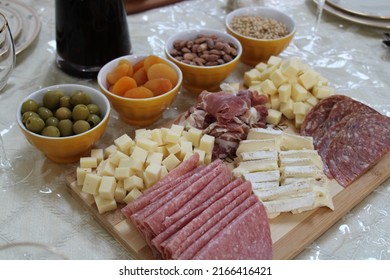 The Top Down, Close Up View Of A Meat And Cheese Platter On Top Of A Dining Room Table. There's A Variety Of Pickings And A Bottle Of Red Wine Next To The Cutting Board.