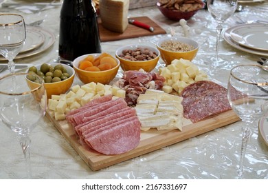 The Top Down, Close Up View Of A Meat And Cheese Platter On Top Of A Dining Room Table. There's A Variety Of Pickings And A Bottle Of Red Wine Next To The Cutting Board.