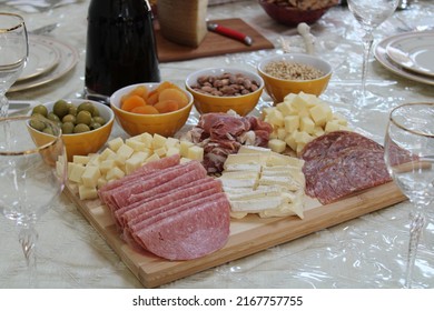 The Top Down, Close Up View Of A Meat And Cheese Platter On Top Of A Dining Room Table. There's A Variety Of Pickings And A Bottle Of Red Wine Next To The Cutting Board.