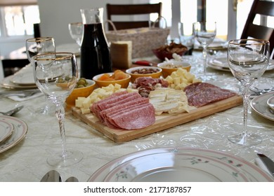 The Top Down, Close Up View Of A Meat And Cheese Platter On Top Of A Dining Room Table. There's A Variety Of Pickings And A Bottle Of Red Wine Next To The Cutting Board.