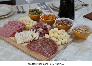 The Top Down, Close Up View Of A Meat And Cheese Platter On Top Of A Dining Room Table. There's A Variety Of Pickings And A Bottle Of Red Wine Next To The Cutting Board.