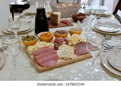 The Top Down, Close Up View Of A Meat And Cheese Platter On Top Of A Dining Room Table. There's A Variety Of Pickings And A Bottle Of Red Wine Next To The Cutting Board.