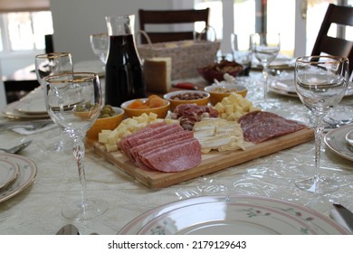 The Top Down, Close Up View Of A Meat And Cheese Platter On Top Of A Dining Room Table. There's A Variety Of Pickings And A Bottle Of Red Wine Next To The Cutting Board.