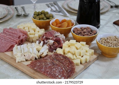 The Top Down, Close Up View Of A Meat And Cheese Platter On Top Of A Dining Room Table. There's A Variety Of Pickings And A Bottle Of Red Wine Next To The Cutting Board.