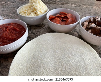 The Top Down, Close Up View Of A Pizza Bar. There Are Frozen Cauliflower Pizza Crusts And Four Bowls Billed With Sauce, Mozzarella Cheese, Pepperoni, And Sliced Mushrooms.