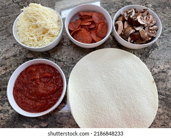 The Top Down, Close Up View Of A Pizza Bar. There Are Frozen Cauliflower Pizza Crusts And Four Bowls Billed With Sauce, Mozzarella Cheese, Pepperoni, And Sliced Mushrooms.