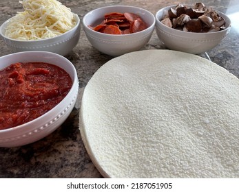 The Top Down, Close Up View Of A Pizza Bar. There Are Frozen Cauliflower Pizza Crusts And Four Bowls Billed With Sauce, Mozzarella Cheese, Pepperoni, And Sliced Mushrooms.