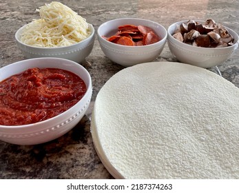 The Top Down, Close Up View Of A Pizza Bar. There Are Frozen Cauliflower Pizza Crusts And Four Bowls Billed With Sauce, Mozzarella Cheese, Pepperoni, And Sliced Mushrooms.