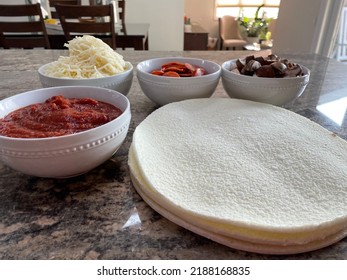 The Top Down, Close Up View Of A Pizza Bar. There Are Frozen Cauliflower Pizza Crusts And Four Bowls Billed With Sauce, Mozzarella Cheese, Pepperoni, And Sliced Mushrooms.