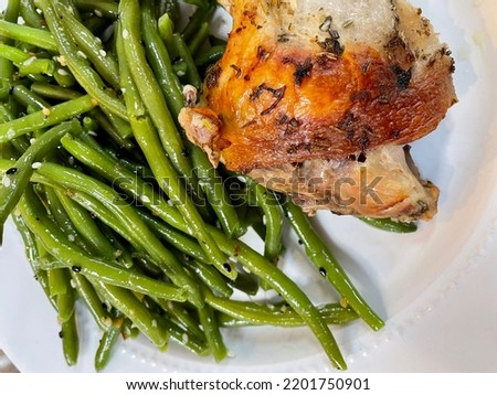 The top down, close up view of a roasted chicken with a side of string beans.