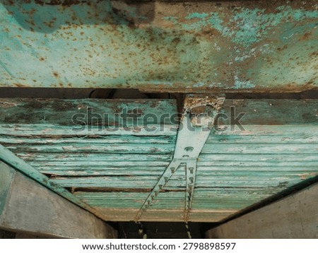 Top down close up view of a weathered turquoise metal sluice gate with peeling paint and rust stains at a rural irrigation dam.