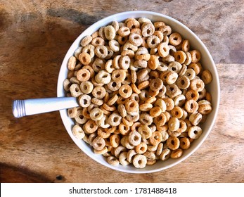 Top Down Closeup View Of Multigrain Hoops (like Cheerios) Cereal On A Wooden Table With Spoon