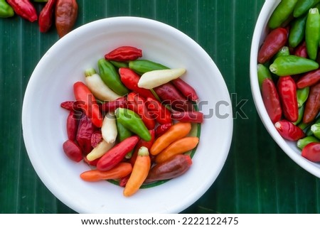 Top down, closeup view of small red, green, orange and creamy white chilli peppers in white dishes on a green banana leaf background. Philippines.