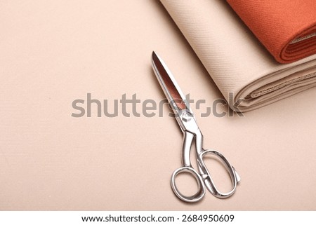 Top down close-up view of soft cashmere wool coating fabric in warm beige and terracotta color perfect for autumn fashion, fall textures, and seasonal textile design. Professional sewing scissors atop