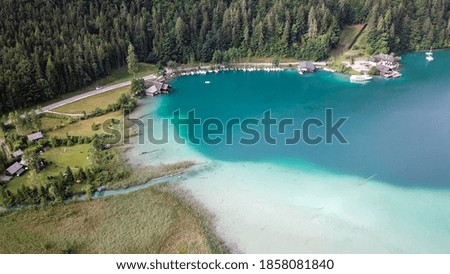 A top down, drone capture of Weissensee lake in Austrian Alps. The water changes color from white, turquoise to navy blue. A small settlement at the shore. A bit of overcast. Serenity and peacefulness