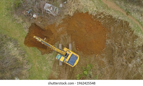 TOP DOWN: Drone Point Of View Of A Large Yellow Excavator Digging A Hole In The Countryside As Part Of Rebuilding An Old Farm. Drone Shot Of An Excavator At Work In A Quiet Rural Area Of Slovenia.