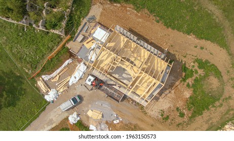 TOP DOWN: Drone Point Of View Of Workers Building The Roof Of A Modern Cross-laminated Timber House Under Construction In The Countryside. Boom Lifts Wooden Beams To The Roof Of Prefabricated House.