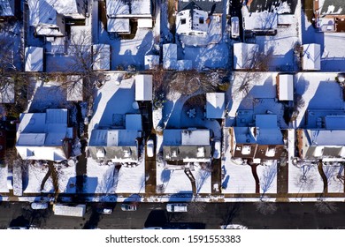 top down drone shot directly over a Long Island NY neighborhood, after a light snowfall in the morning. No one is around and the shadows of the homes are seen on the fresh snow