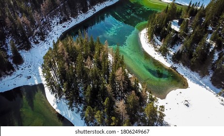 Ein Top-Down-Drohnenschuss vom Grünen See in den österreichischen Alpen. Der See glänzt mit vielen Grün- und Türkistönen. Dickiger Wald um ihn herum. Winter in den Bergen. Es ist Schnee auf dem Boden. Wandern