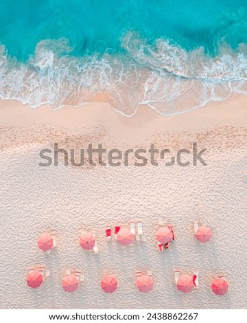 top down drone view of pink umbrellas and chairs on soft white sand beach with blue waves crashing on shore
