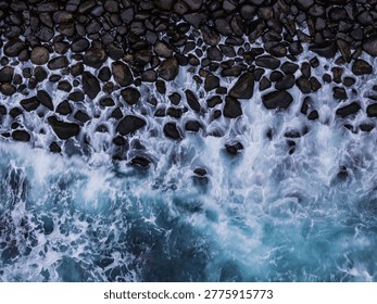 Top down drone view of waves washing over stone pebble beach. Water texture and foam details background footage