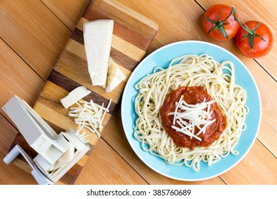 Top Down First Person Perspective View On Blue Plate Of Spaghetti Topped With Red Sauce And Grated Gruyere Cheese Next To Pasta Press And Two Tomatoes