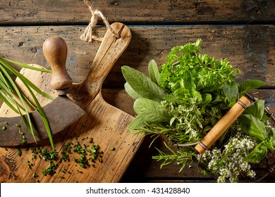 Top Down First Person Perspective View On Various Herbs In Basket Beside Cutting Board On Table For Food Preparation