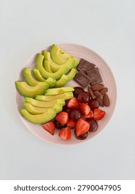 A top down (flat lay) high angle photograph showcasing a nutritious and healthy snack plate beautifully arranged on a clean, minimalist white surface