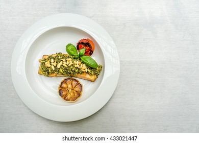 Top Down Flat Lay Image Of Grilled Salmon With Pesto Sauce Garnished With Baked Sunflower Seeds, Garlic, Grilled Tomato And Basil Leave. A Delicious Italian Food Dish With Asian Touch