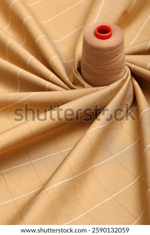 Top down flat lay photo of beige, plaid, wool, fashion fabric on designers table. Sewing thread on top of the fabric.