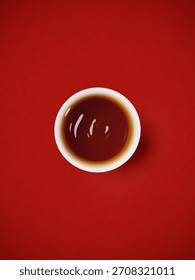 Top down flat lay view of white ceramic cup filled with dark oolong tea isolated on textured red background      