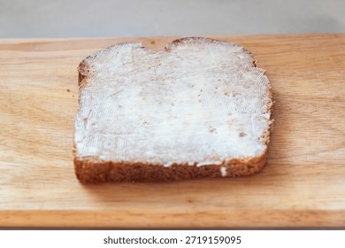 Top down flat lay view of a single slice of brown toast covered with distinct knife marks of butter spread placed centrally on a light wooden board representing a classic breakfast preparation