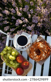 Top down flat lay view of a cozy breakfast in blooming lavender field. White cup of black coffee, fresh grapes, peaches and almond sweet pastry